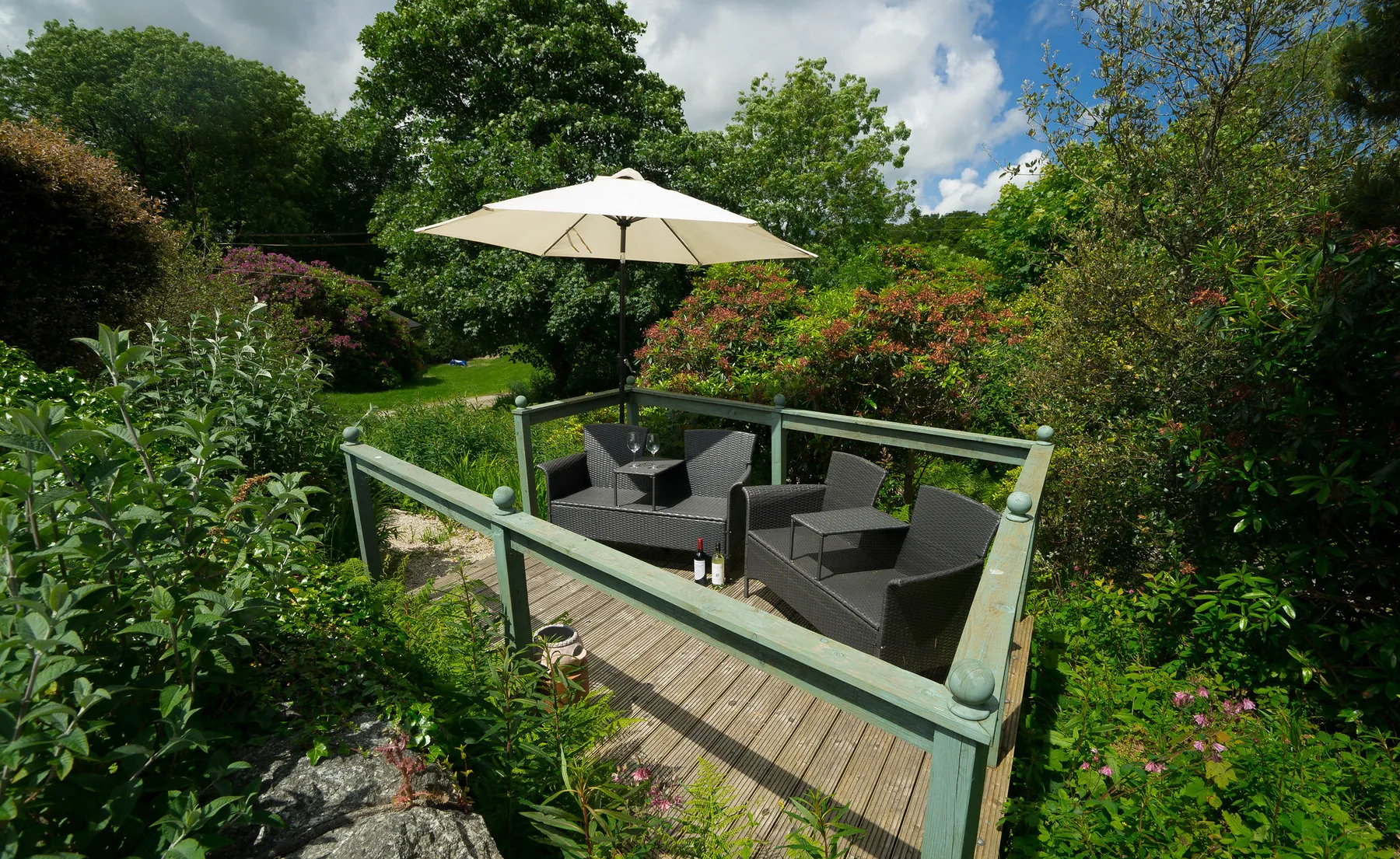 Sheltered garden seating with a parasol beside the pond at Higher Faugan Parc